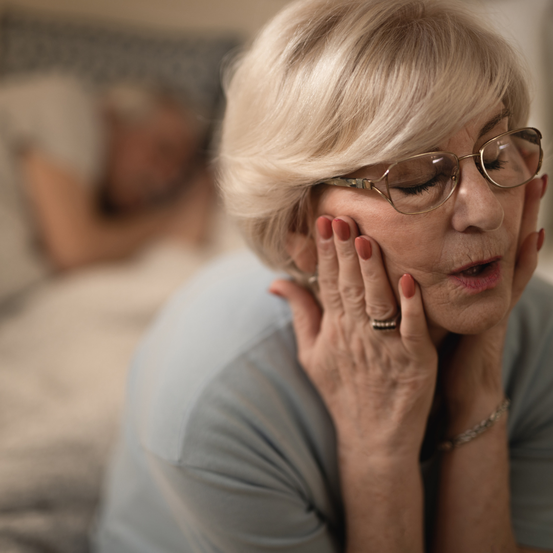 Lady with spinal stenosis, head in her hands sat on the edge of her bed unable to sleep.